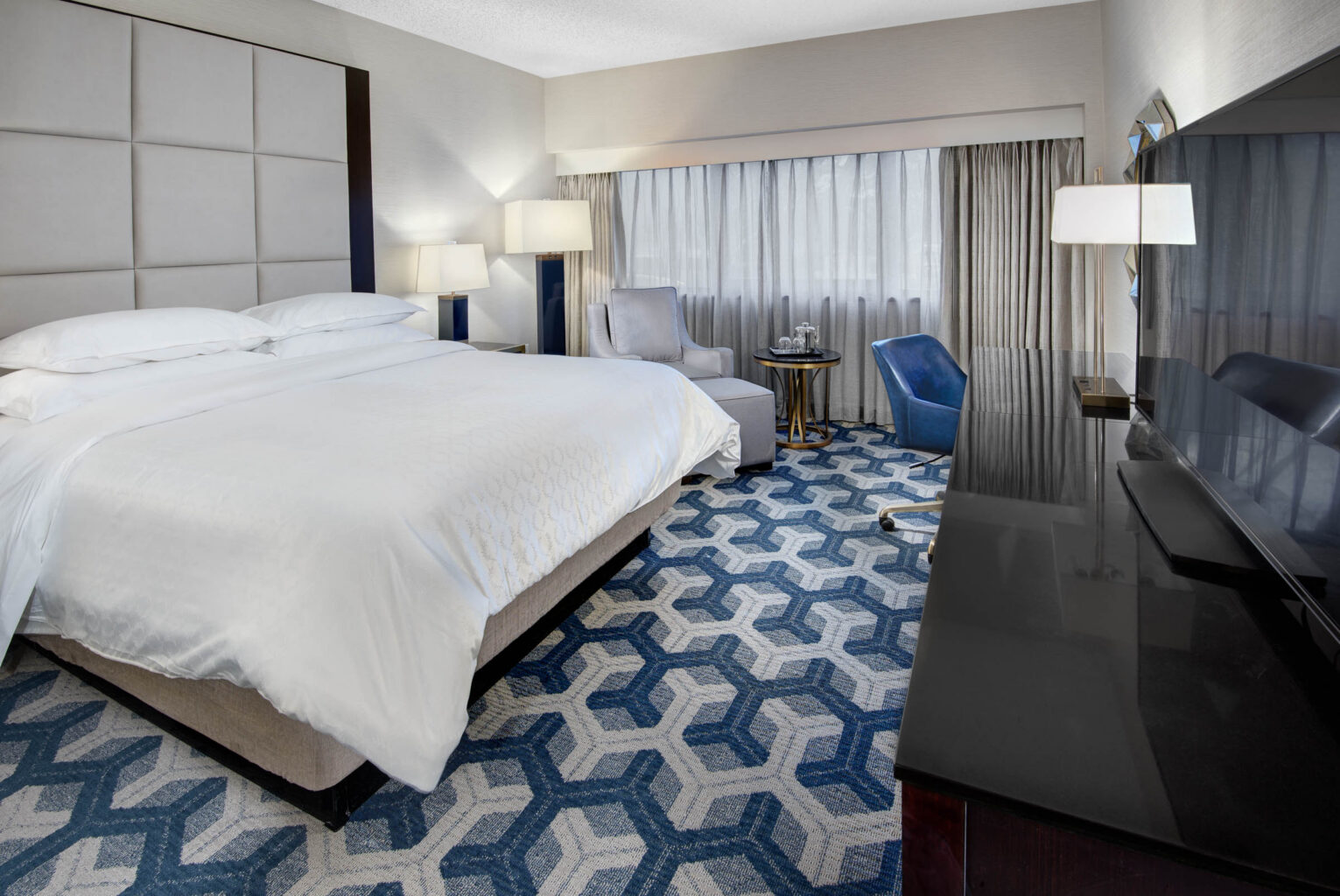 modern hotel room with white linens blue carpet and other amenities